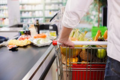 man in white shirt pushing cart through grocery store checkout lane