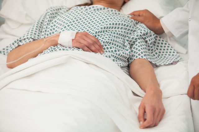 hospitalized woman in bed with hand on shoulder
