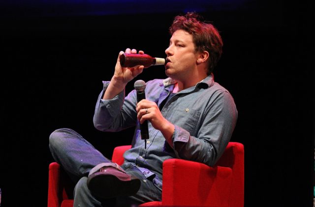 jamie oliver in a chambray shirt and jeans drinking a beer