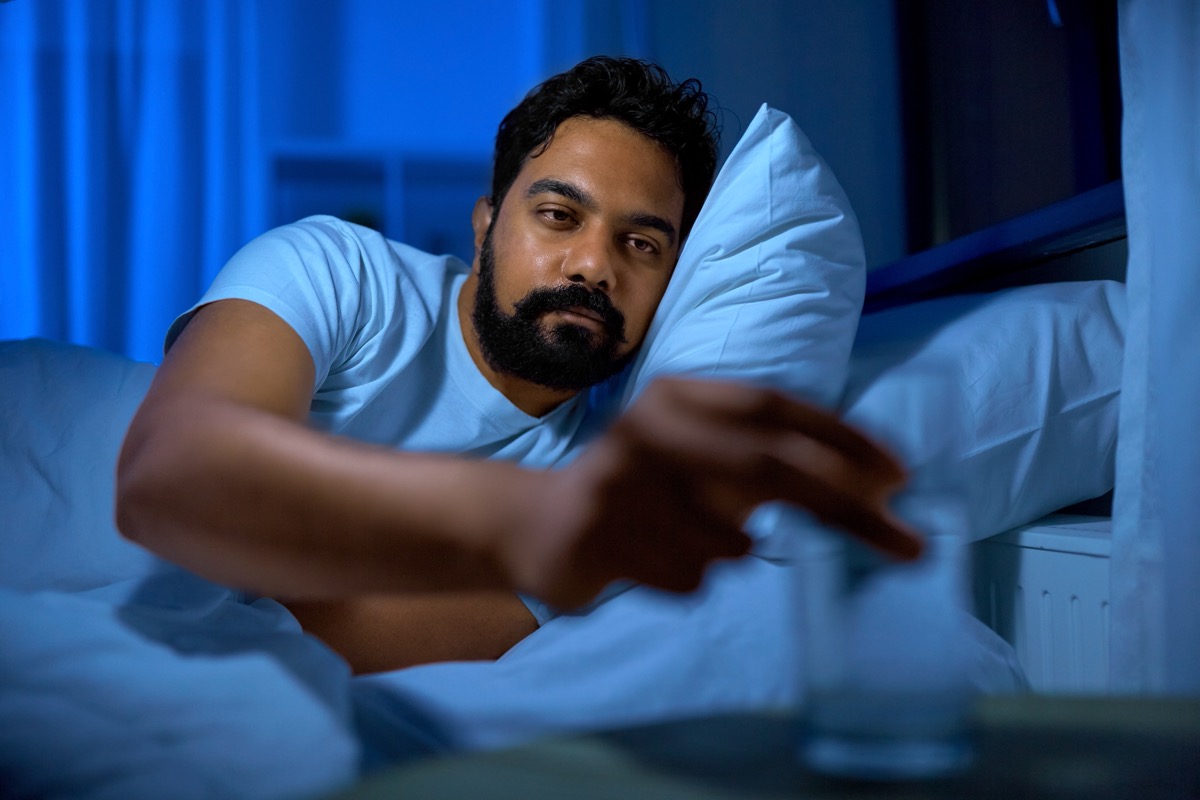 man drinking a glass of water in bed at nighttime