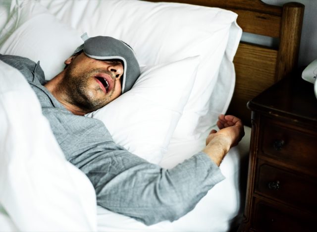 middle aged man in gray shirt and sleep mask sleeping with mouth open