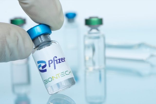 Glass bottle with logo Pfizer and BioNTech in the doctor's hand.