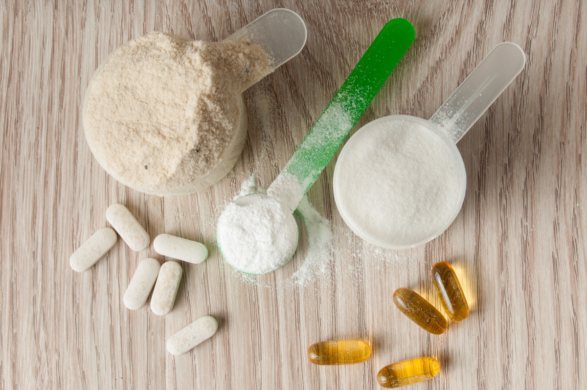 Scoop of protein, bcaa and creatine, omega3 in pills on wooden background.