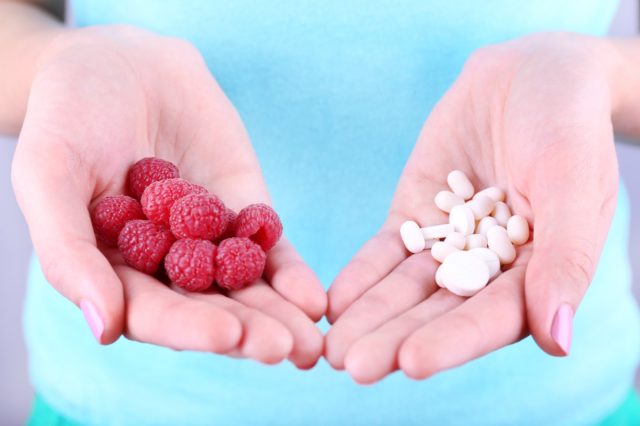 Woman holding berries and pills on grey background