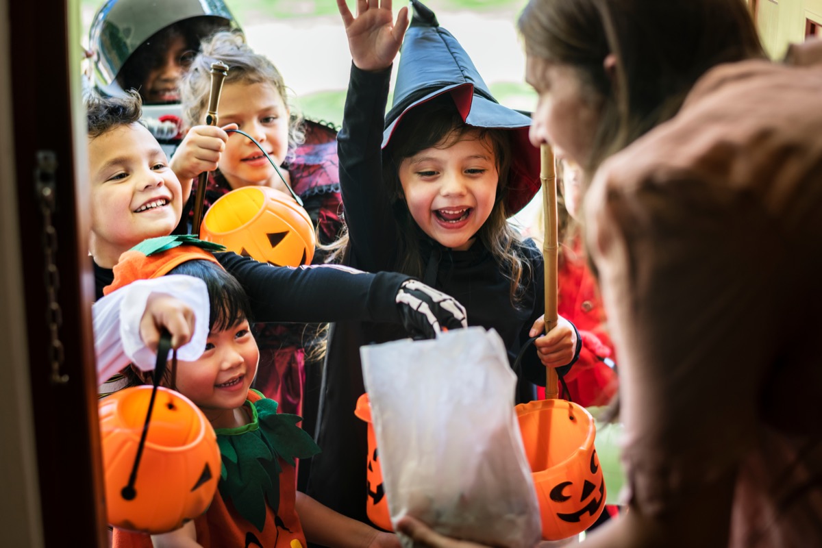woman handing out candy to trick or treaters in costume on halloween