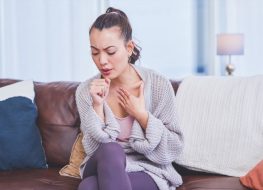 Young woman sitting alone on her sofa at home and coughing.