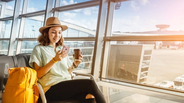 young woman in fedora drinking coffee at airport