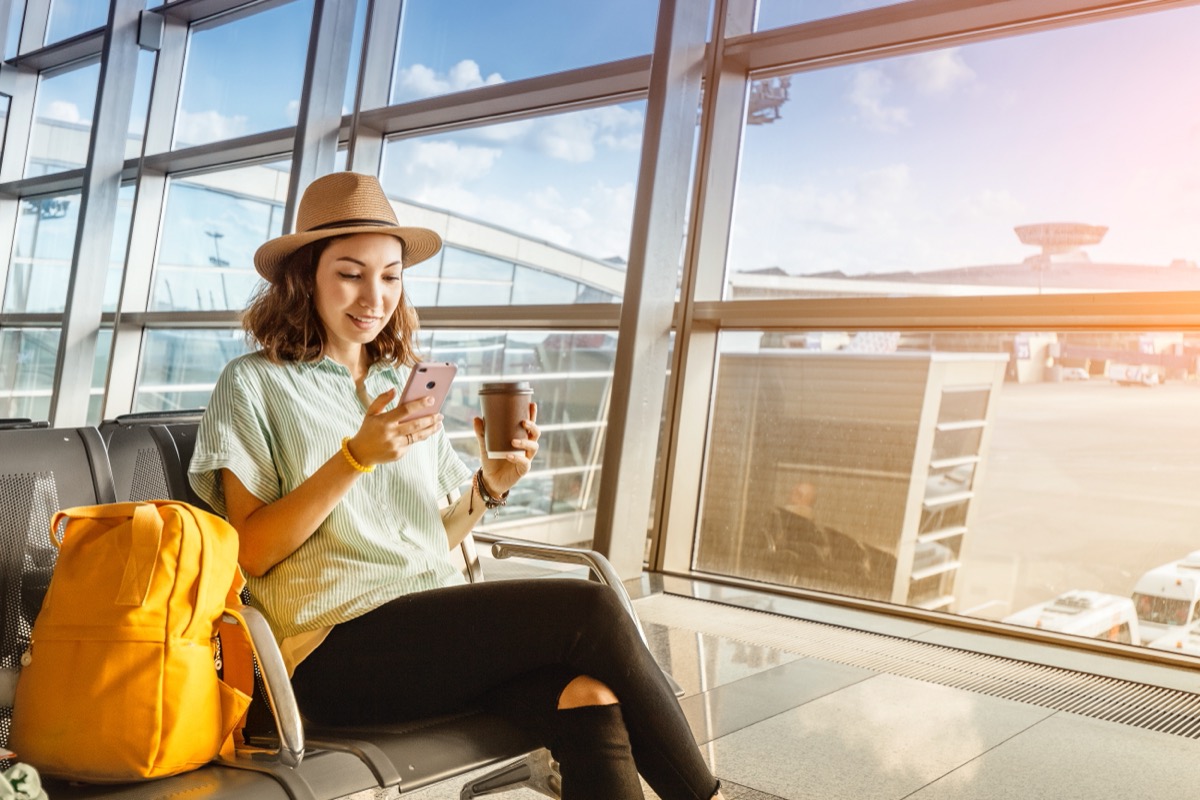 young woman in fedora drinking coffee at airport