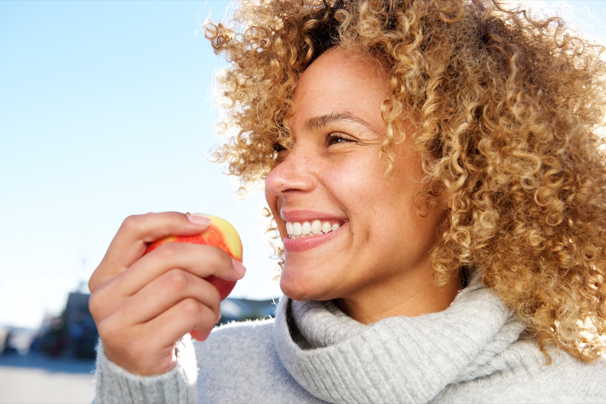 young woman in turtleneck eating apple outdoors