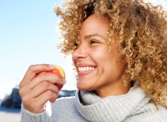 young woman in turtleneck eating apple outdoors
