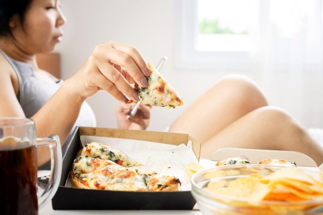 Femme mange de la pizza au lit