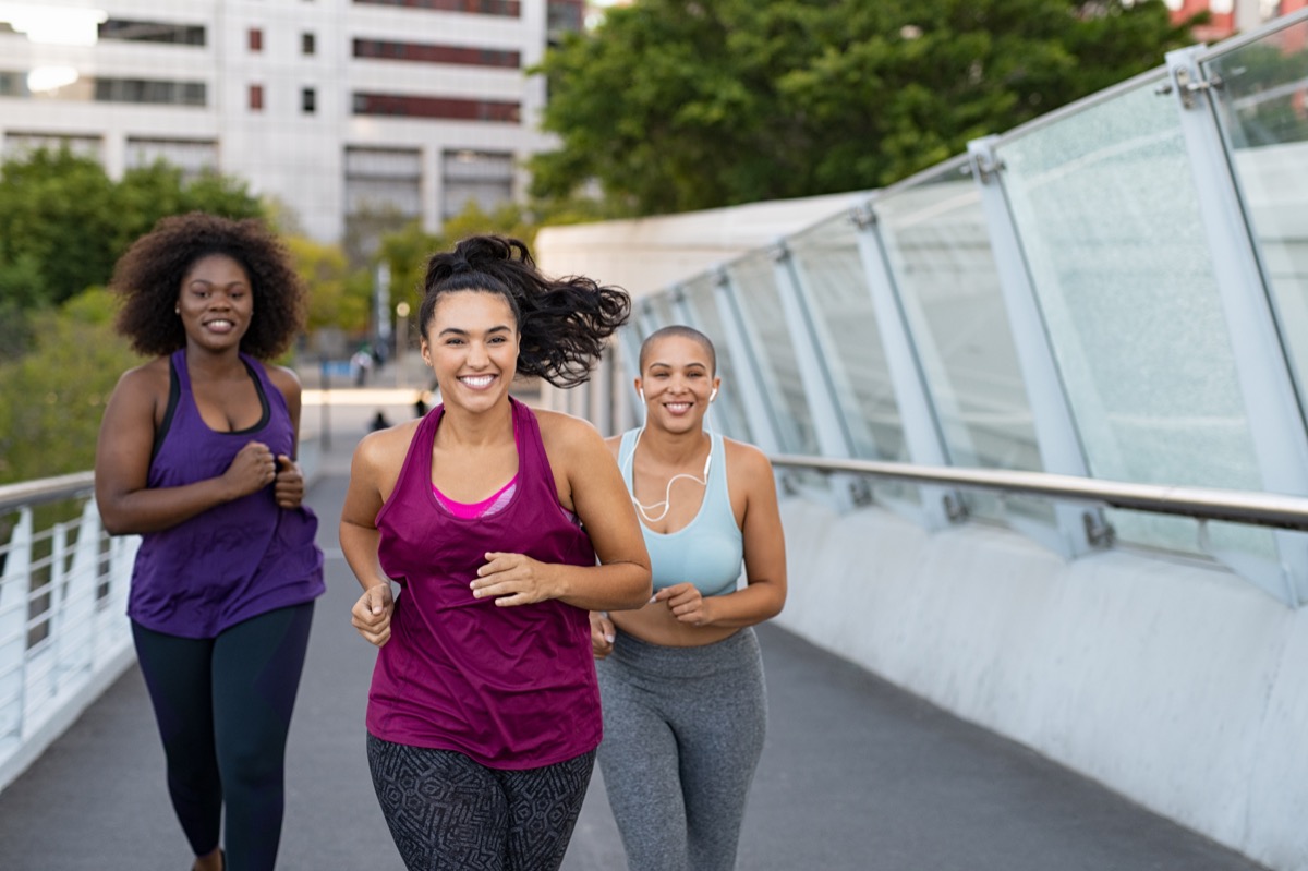 group of young, attractive multiracial women running in tank tops and leggings across a modern bridge