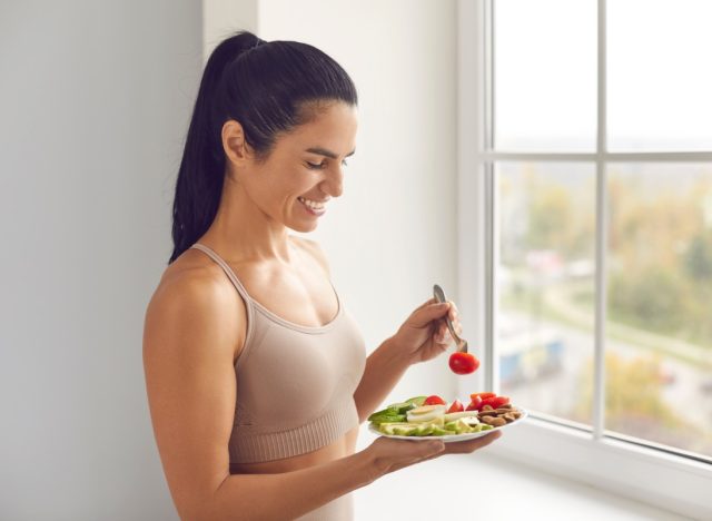 young woman in tan top and ponytail eating a healthy meal in front of a window