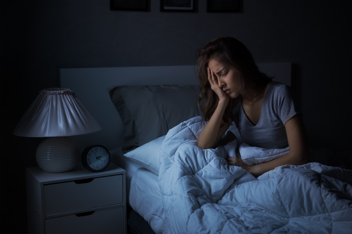 young woman holding face in bed in the dark dealing with insomnia or poor sleep