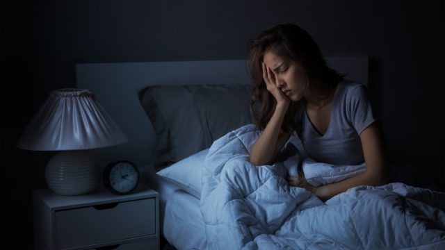 young woman holding face in bed in the dark dealing with insomnia or poor sleep