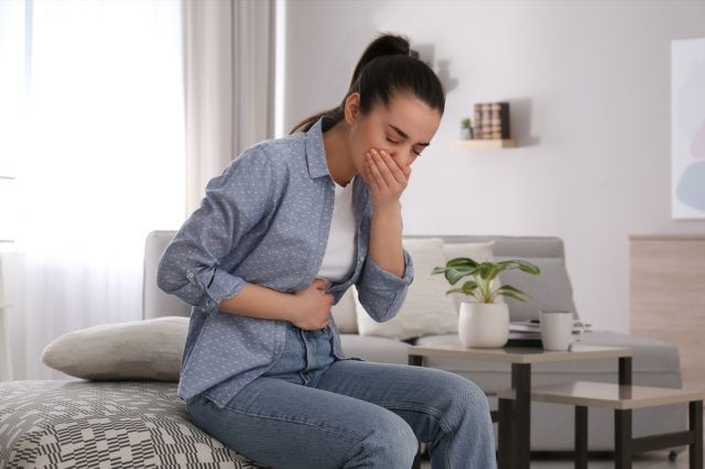 young woman with nausea in denim outfit sitting on the bed