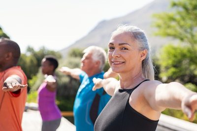 happy older woman smiling while doing outdoor yoga in a group