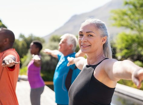 happy older woman smiling while doing outdoor yoga in a group