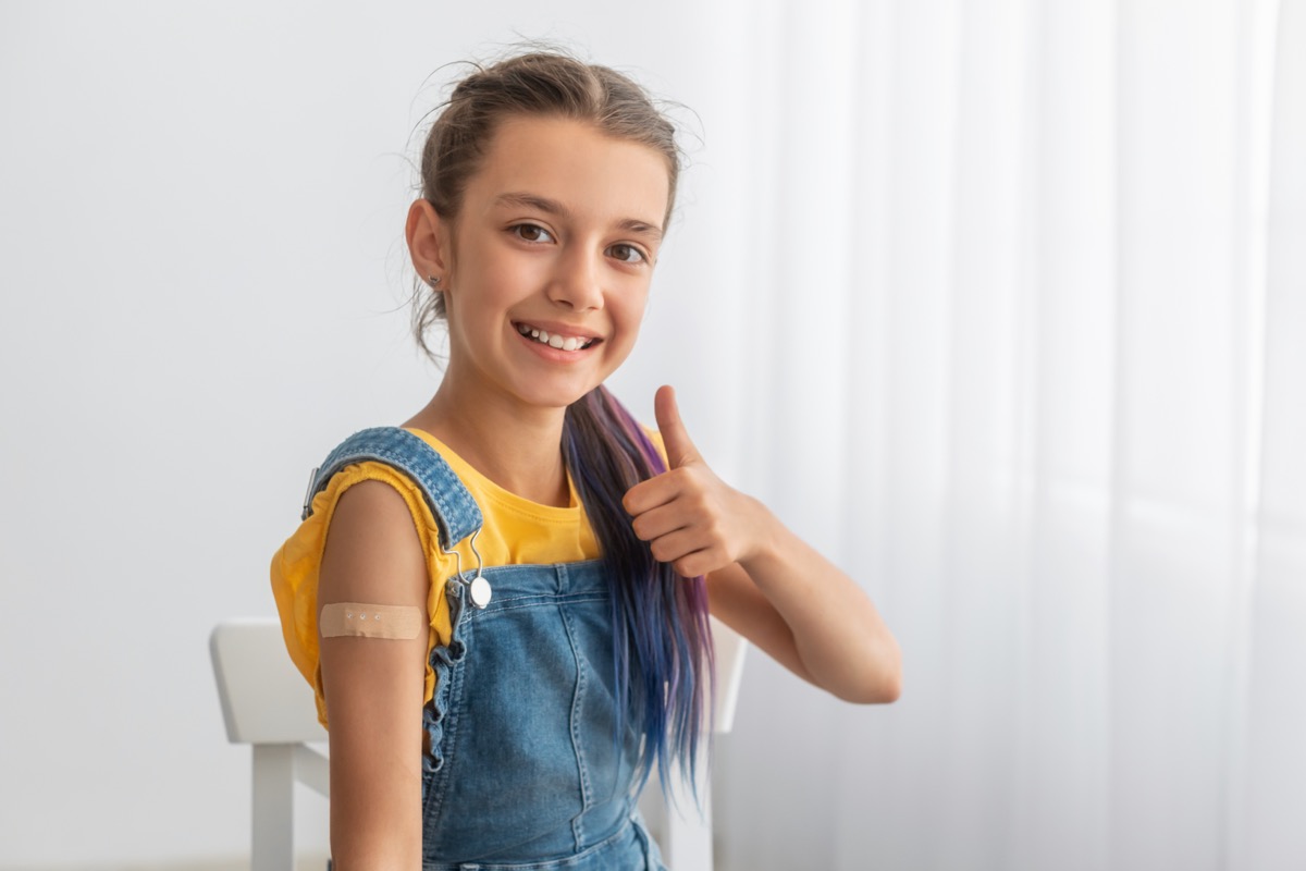 Cheerful Smiling Adolescent Patient Showing Vaccinated Arm With Sticking Patch On Her Shoulder After Getting Shot And Thumb Up Gesture.