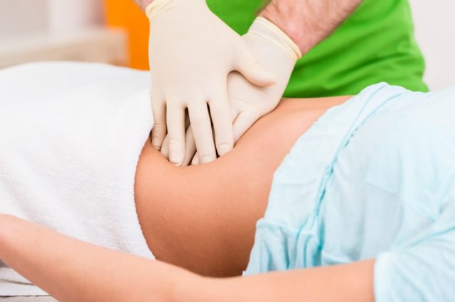 Practitioner at colon therapy massaging abdomen wall of woman