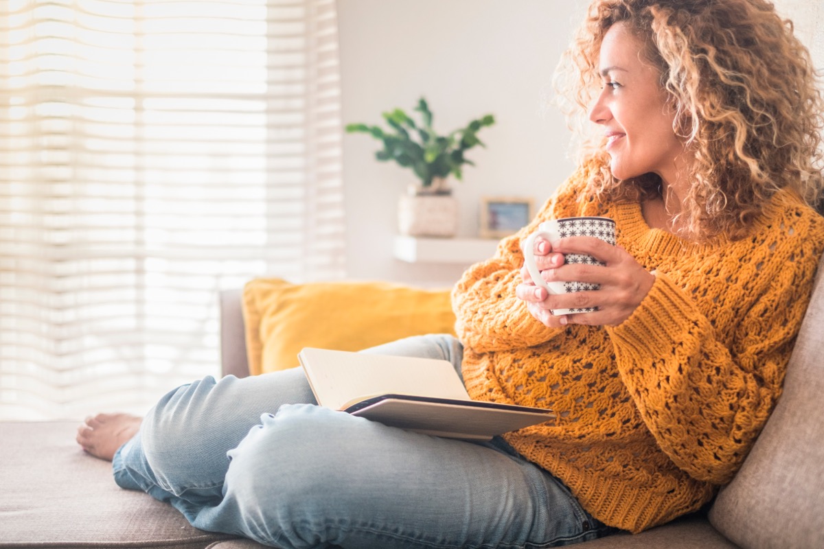 curly haired woman drinking from mug while sitting on couch
