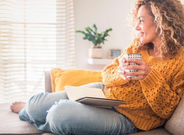 curly haired woman drinking from mug while sitting on couch