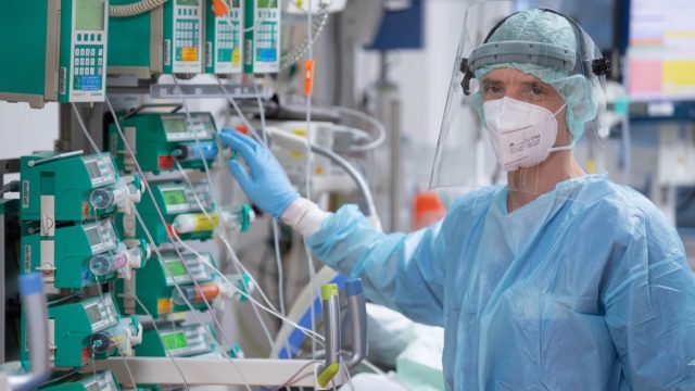 intensive care nurse, stands at the bedside of a young corona patient in the intensive care unit.