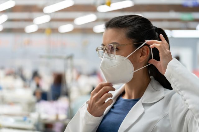 Woman working textile factory during the COVID-19 pandemic and fixing her facemask