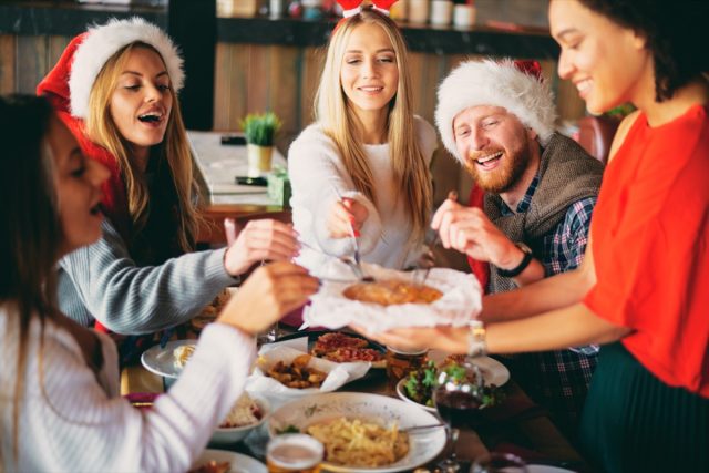 group of 20- or 30-something friends eating holiday meal together in santa hats