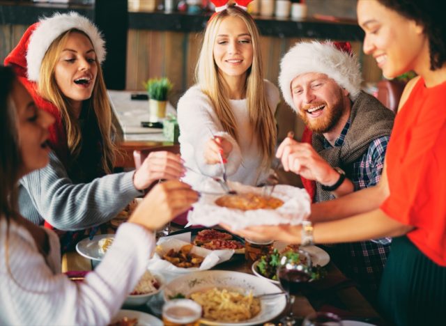 group of 20- or 30-something friends eating holiday meal together in santa hats