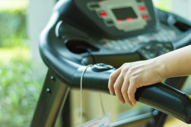 person walking on treadmill while holding handrails