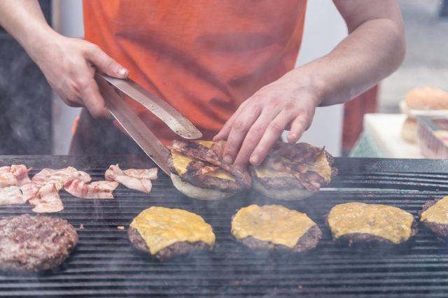 person grilling burgers with cheese and bacon on large grill