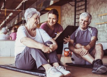 older couple talking to personal trainer in gym setting