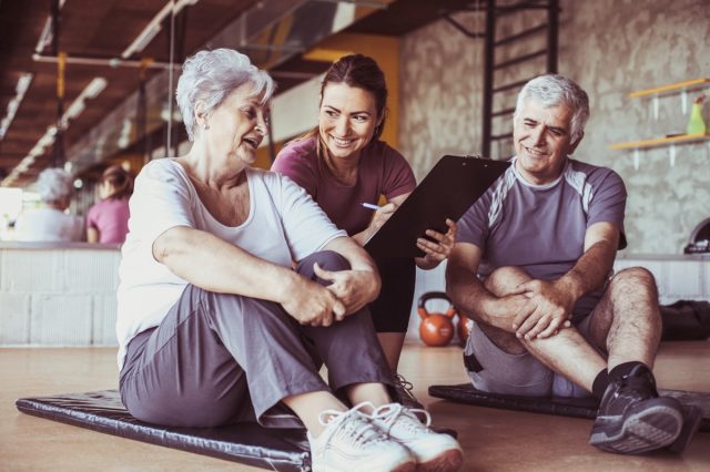 older couple talking to personal trainer in gym setting