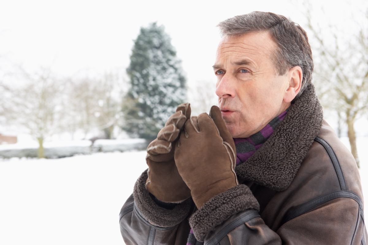 older man blowing on gloved hands outside in snow