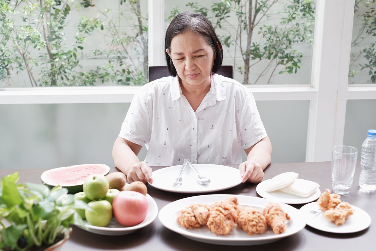 older woman who is not feeling hungry looking at plates of food