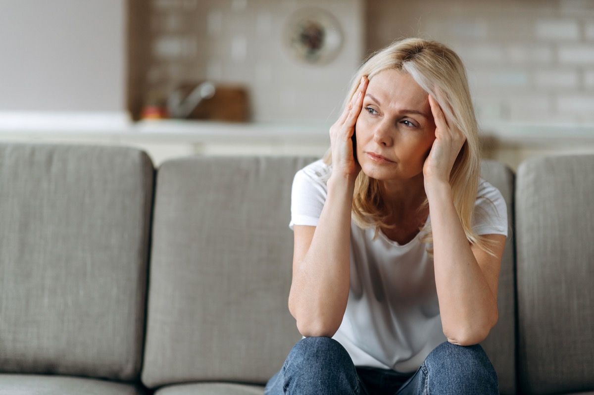 Sad caucasian senior woman wearing casual clothes sits on couch at home alone