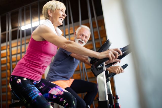 happy senior couple cycling on exercise bikes