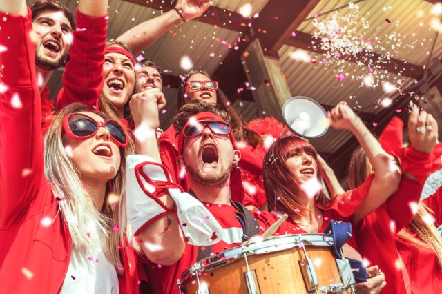 A group of fans dressed in red color watching a sports event in the stands of a stadium.