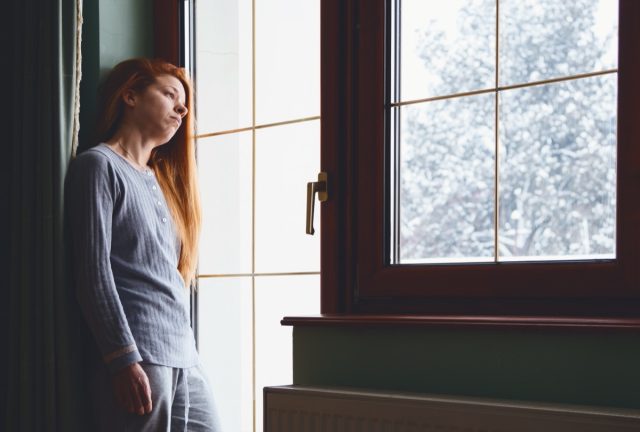 sad woman with winter depression looking out window