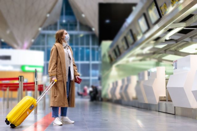 Woman with luggage stands at almost empty check-in counters at the airport terminal due to coronavirus pandemic/Covid-19 outbreak travel restrictions.