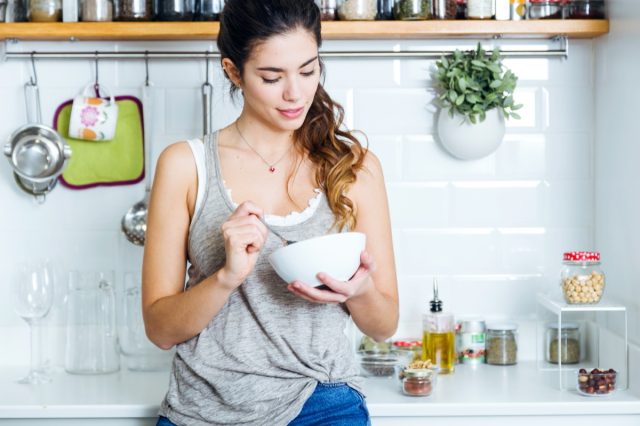young woman eating cereal in kitchen