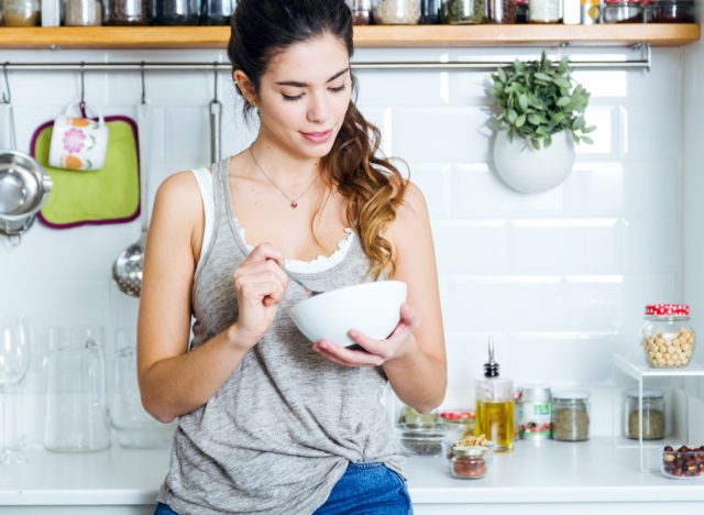 young woman eating cereal in kitchen
