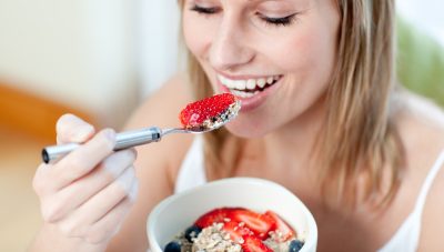 young blonde woman eating berries and oatmeal