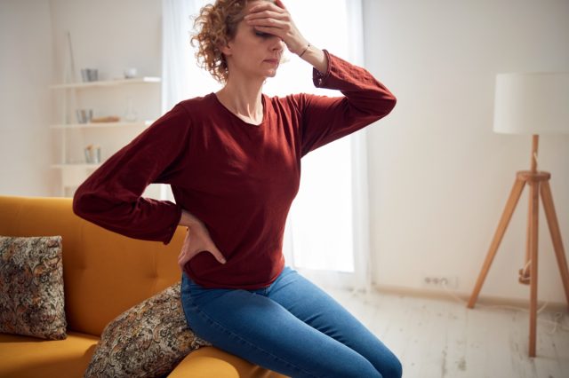 Woman with head and hip pain sitting on a couch at home.