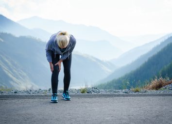 woman with knee pain walking on a trail with mountains behind her