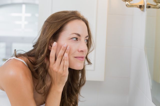 Woman examining her face in the mirror in the bathroom.