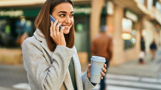 young woman drinking coffee outdoors while on cell phone