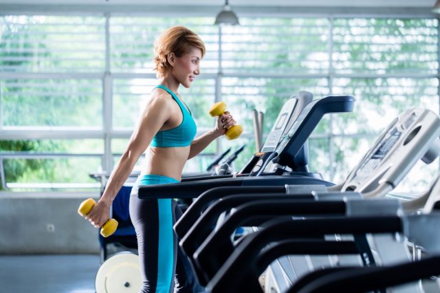 Woman running on treadmill holding weights in hand