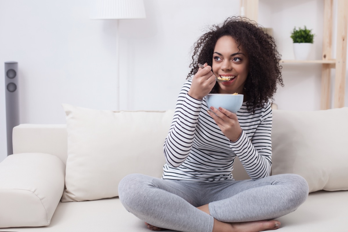 young woman eating from bowl on couch